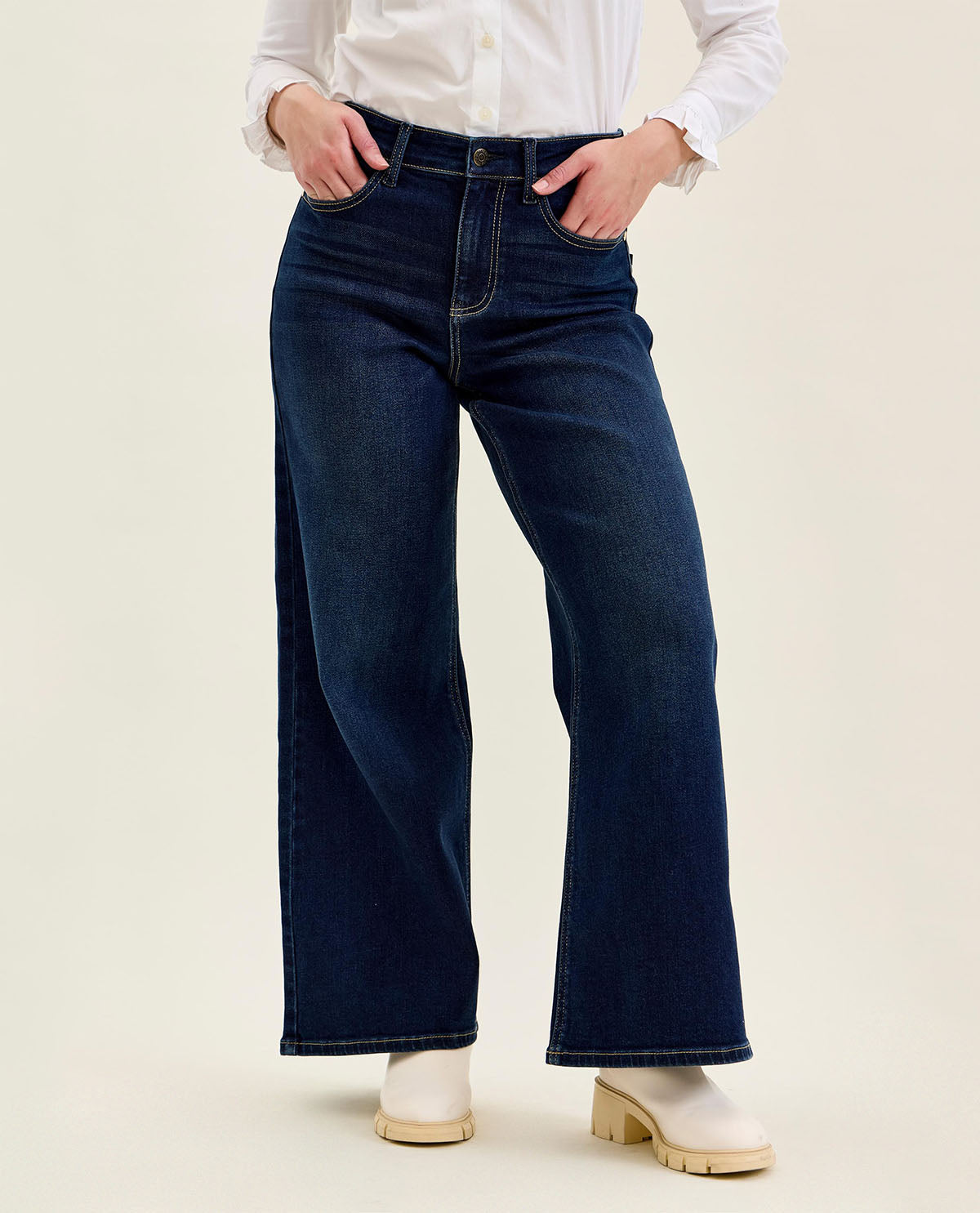 Person wearing dark blue wide-leg jeans and a white shirt on a beige background