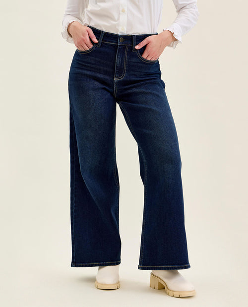 Person wearing dark blue wide-leg jeans and a white shirt on a beige background