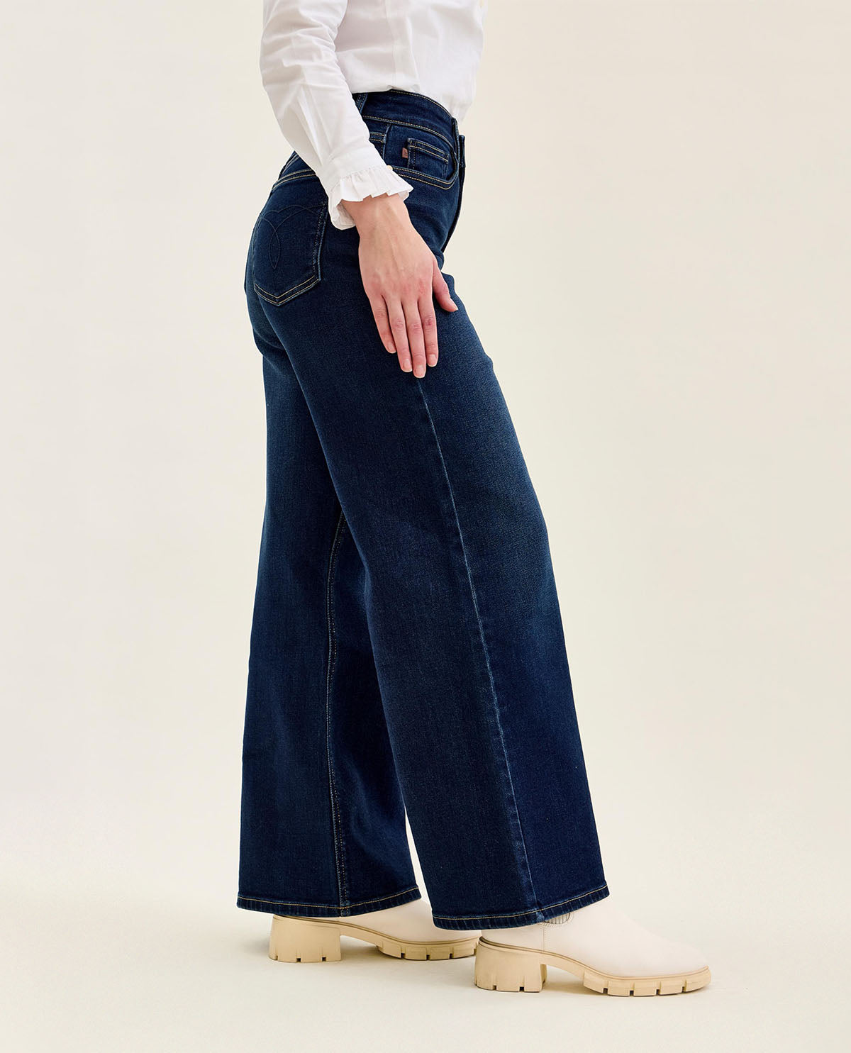Person wearing dark blue wide-leg jeans and a white shirt on a beige background