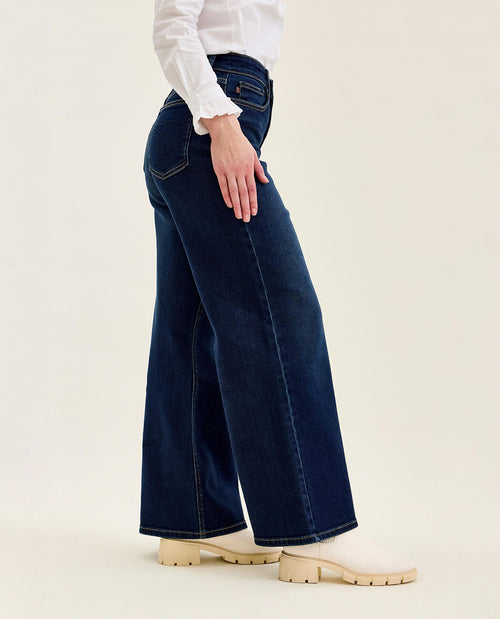 Person wearing dark blue wide-leg jeans and a white shirt on a beige background
