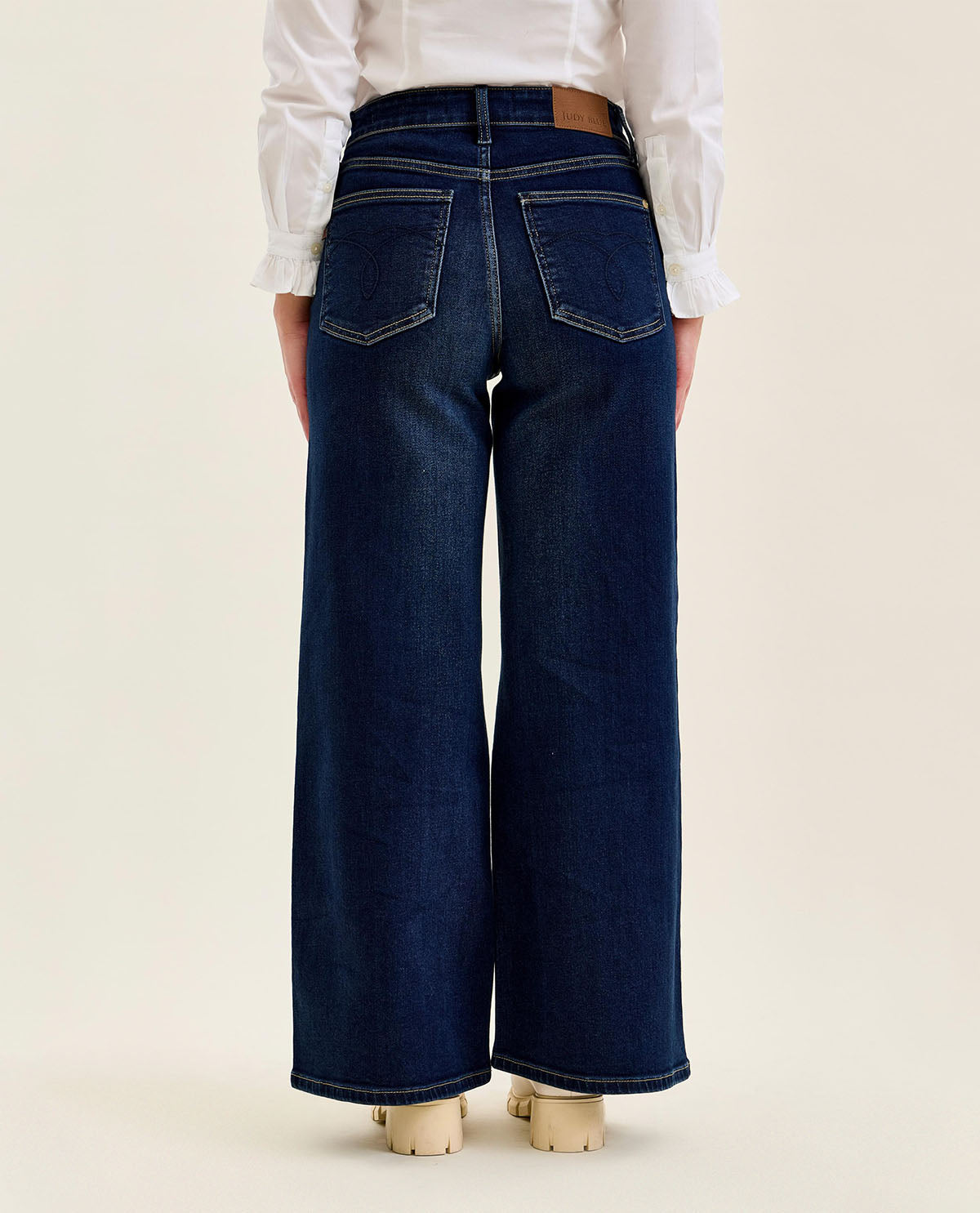 Person wearing dark blue wide-leg jeans on a beige background