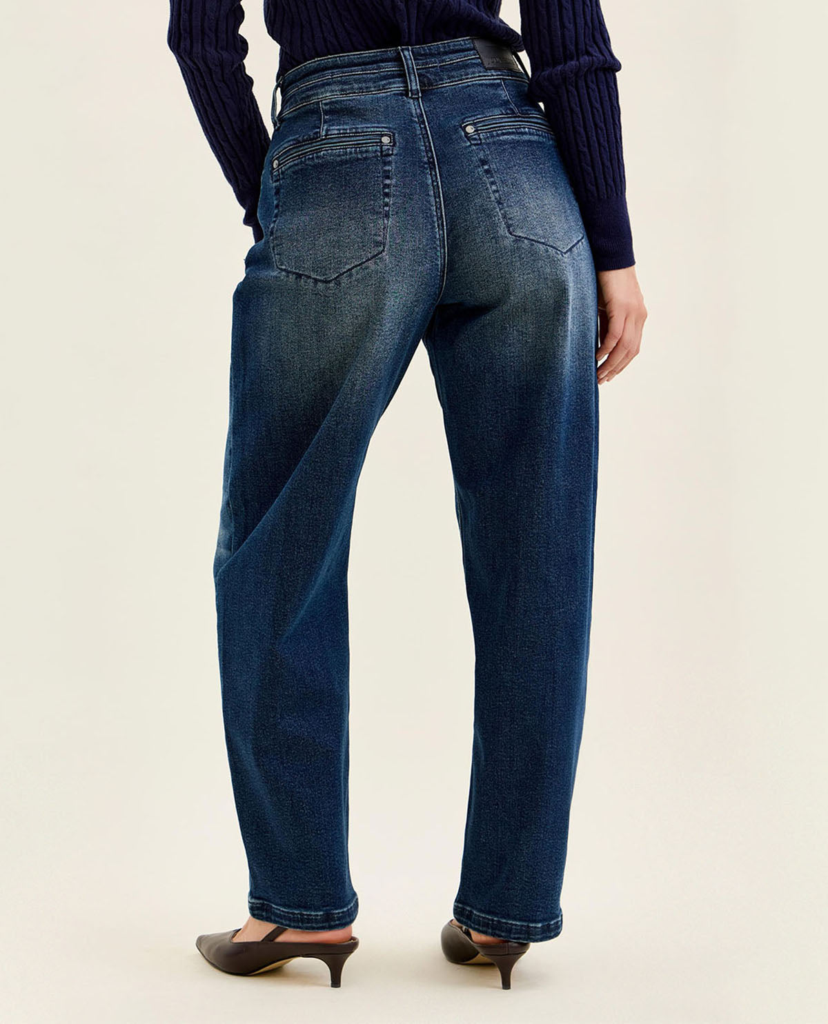Person wearing blue jeans and a dark sweater on a beige background