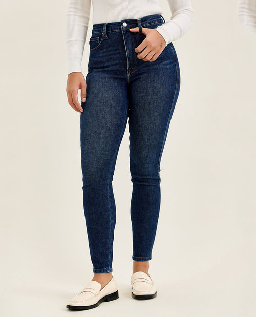 Person wearing dark blue jeans and white shoes on a plain background