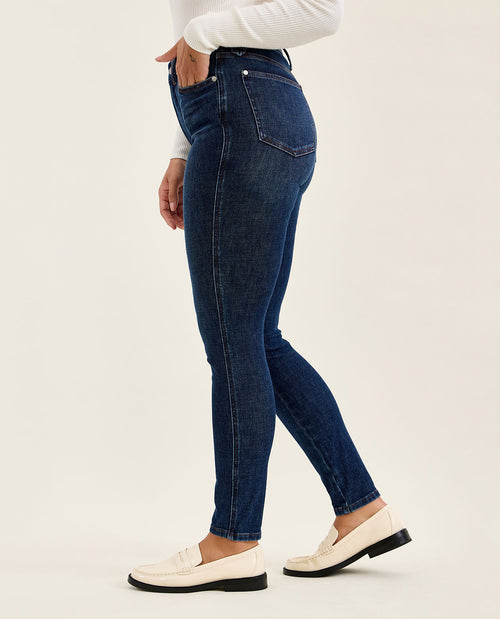 Person wearing dark blue jeans and white shoes on a light background