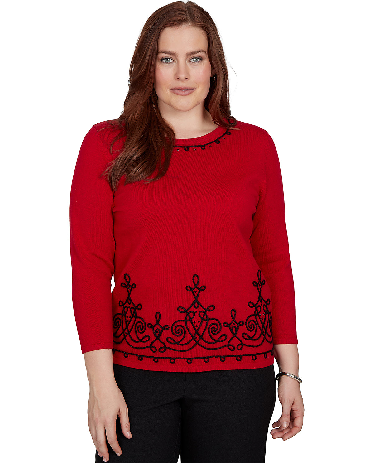 A woman modeling a bright red long-sleeve knit top with black embroidered scrollwork along the hem and neckline, paired with black pants, against a plain white background.