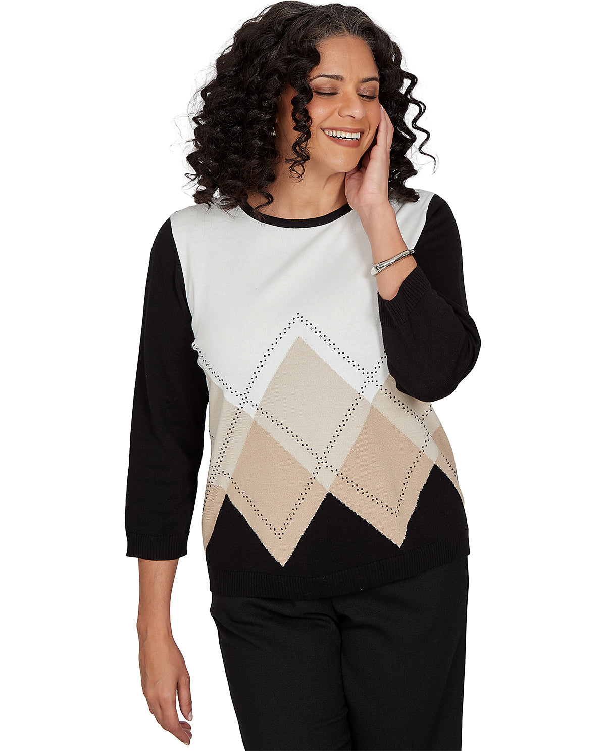 A woman wearing a three-quarter sleeve knit top with a color-blocked design. The top features a white upper yoke, black sleeves and lower body, and a beige argyle pattern across the center.