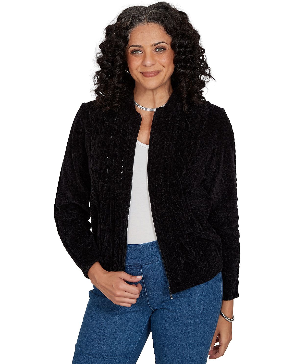 A woman with curly dark hair wearing a black textured zip-up jacket over a white top and blue jeans, photographed against a plain white background.