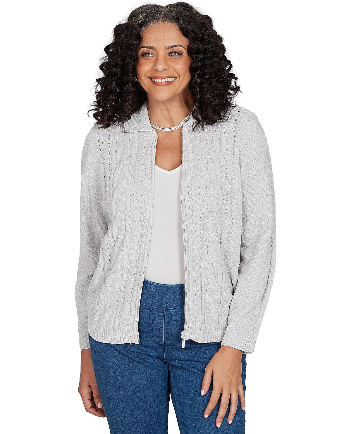 A woman with curly dark hair wearing a light gray cable-knit zip-front cardigan over a white top and blue jeans, photographed against a plain white background.