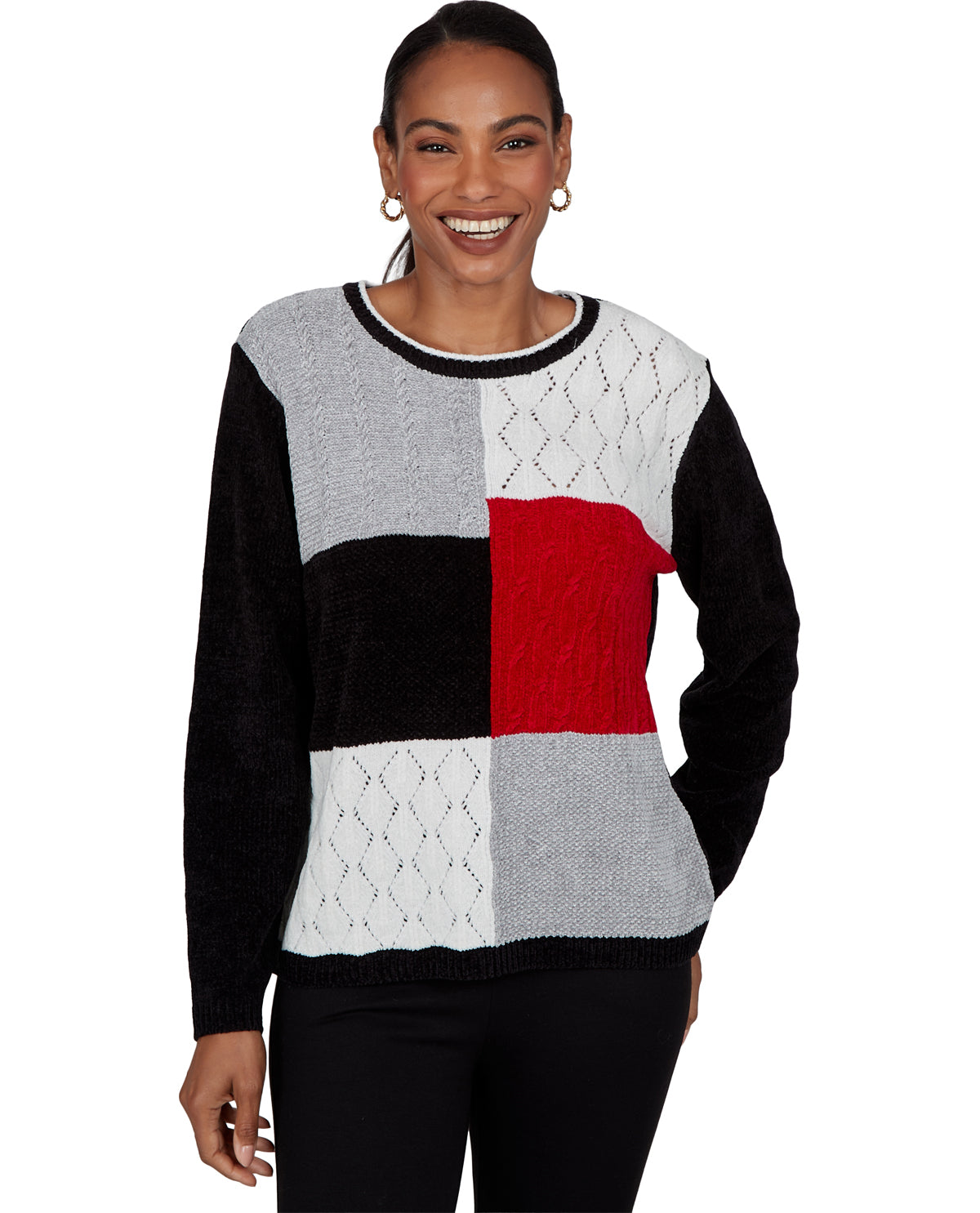 A woman wearing a color-block knit sweater with black, light gray, white, and red panels, paired with black pants, against a plain white background.