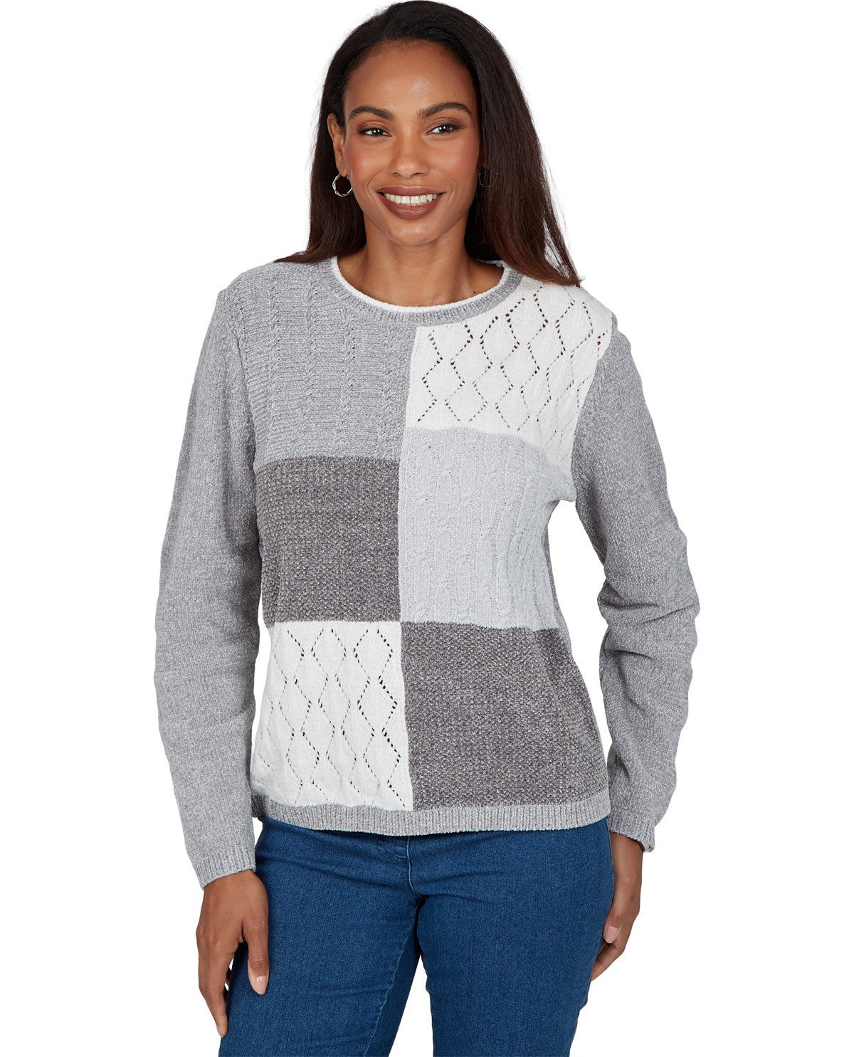 A woman wearing a gray and white patchwork knit sweater with blue jeans, photographed against a plain white background.