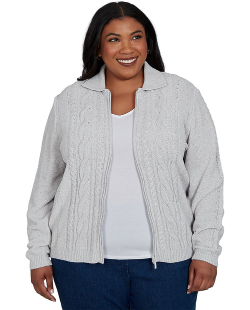 A smiling woman wearing a light gray cable-knit zip-up cardigan over a white top and blue jeans, photographed against a plain white background.