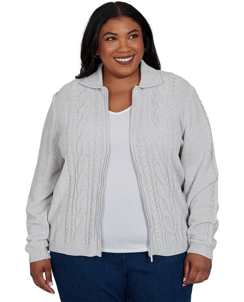 A smiling woman wearing a light gray cable-knit zip-up cardigan over a white top and blue jeans, photographed against a plain white background.