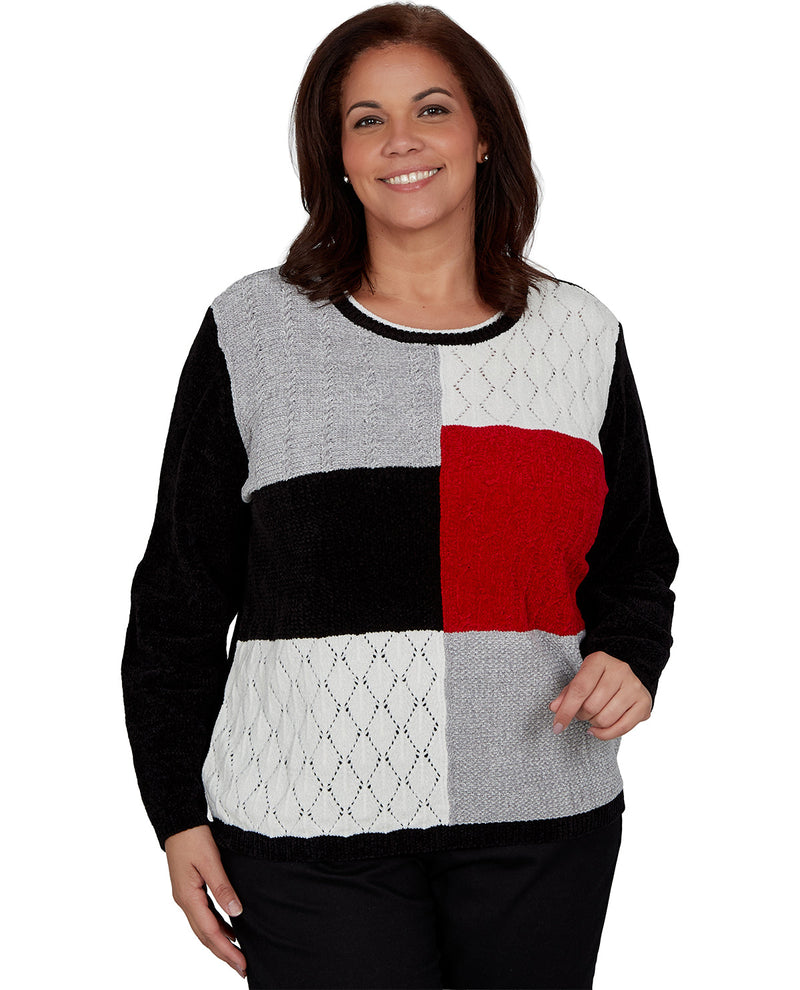 A woman wearing a color-blocked knit sweater with black, light gray, white, and red panels, paired with black pants, against a plain white background.