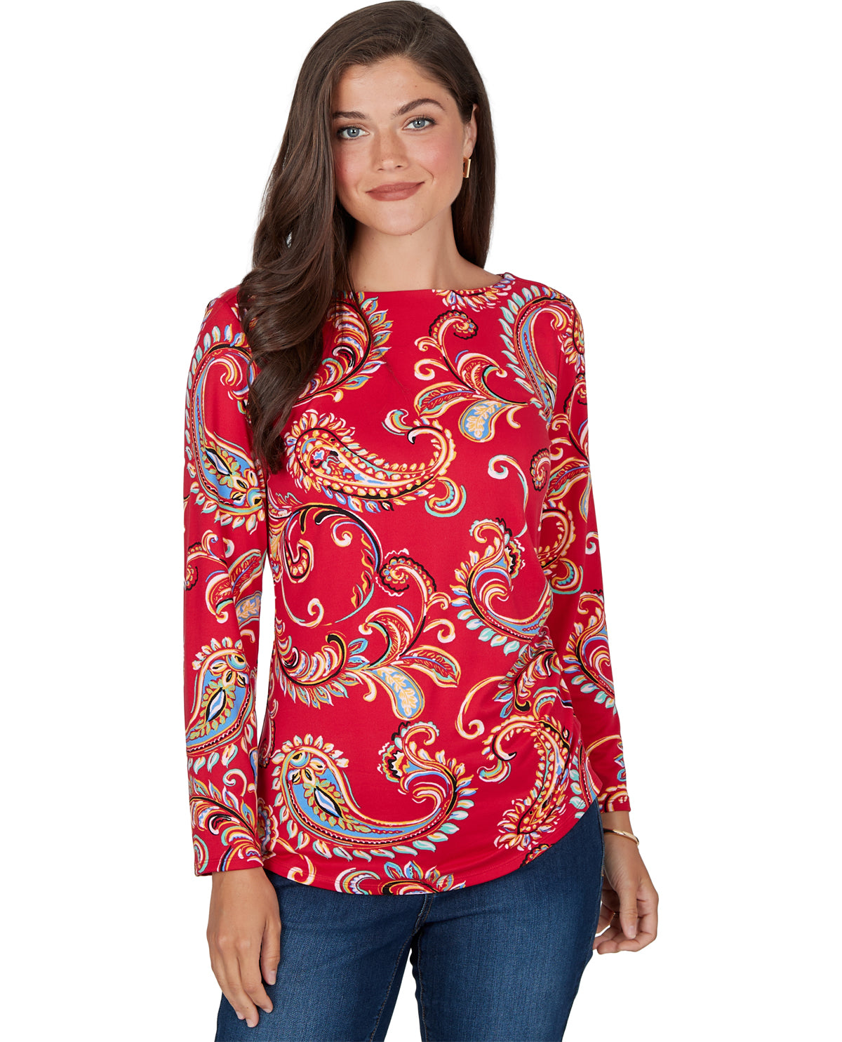 A woman modeling a red long-sleeve top with a vibrant paisley pattern in orange, blue, and white, paired with blue jeans against a plain white background.