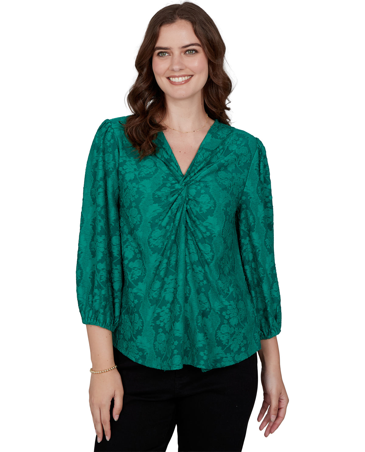 A woman wearing a green floral jacquard blouse with a gathered front and 3/4 sleeves, paired with black pants, against a plain white background.
