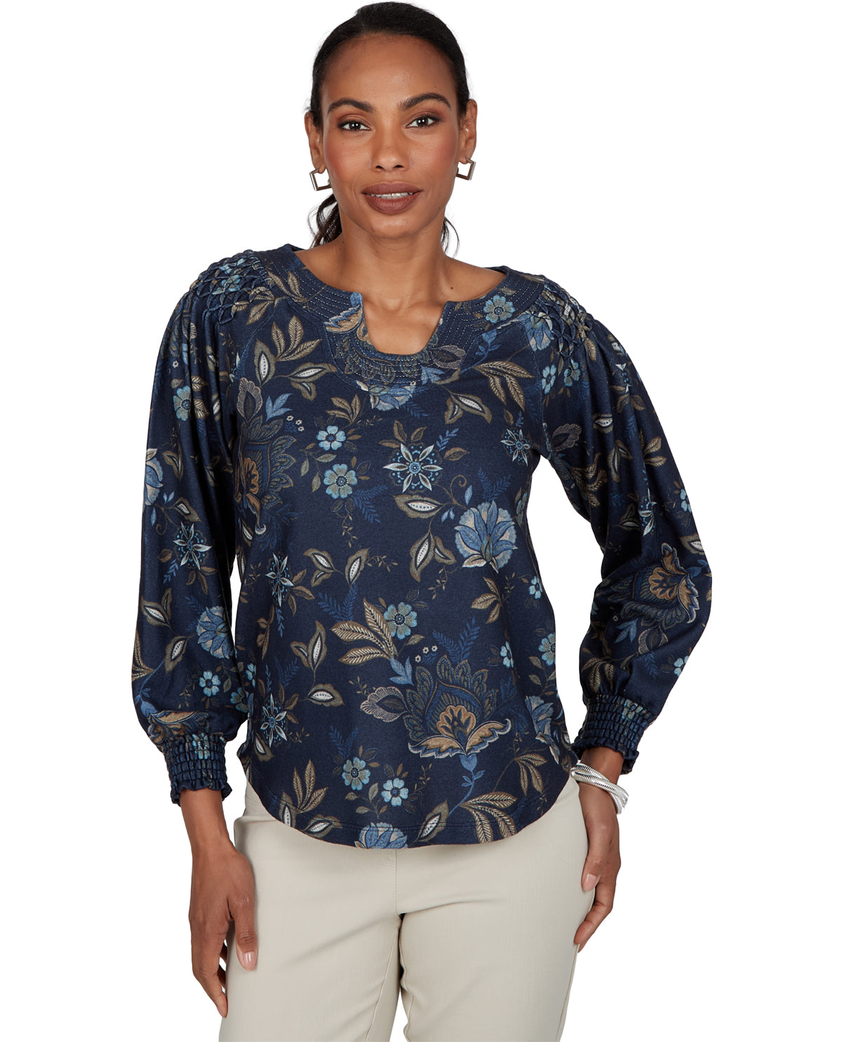A woman modeling a navy blue long-sleeve blouse with a blue, beige, and white floral pattern, paired with light beige pants, against a plain white background.