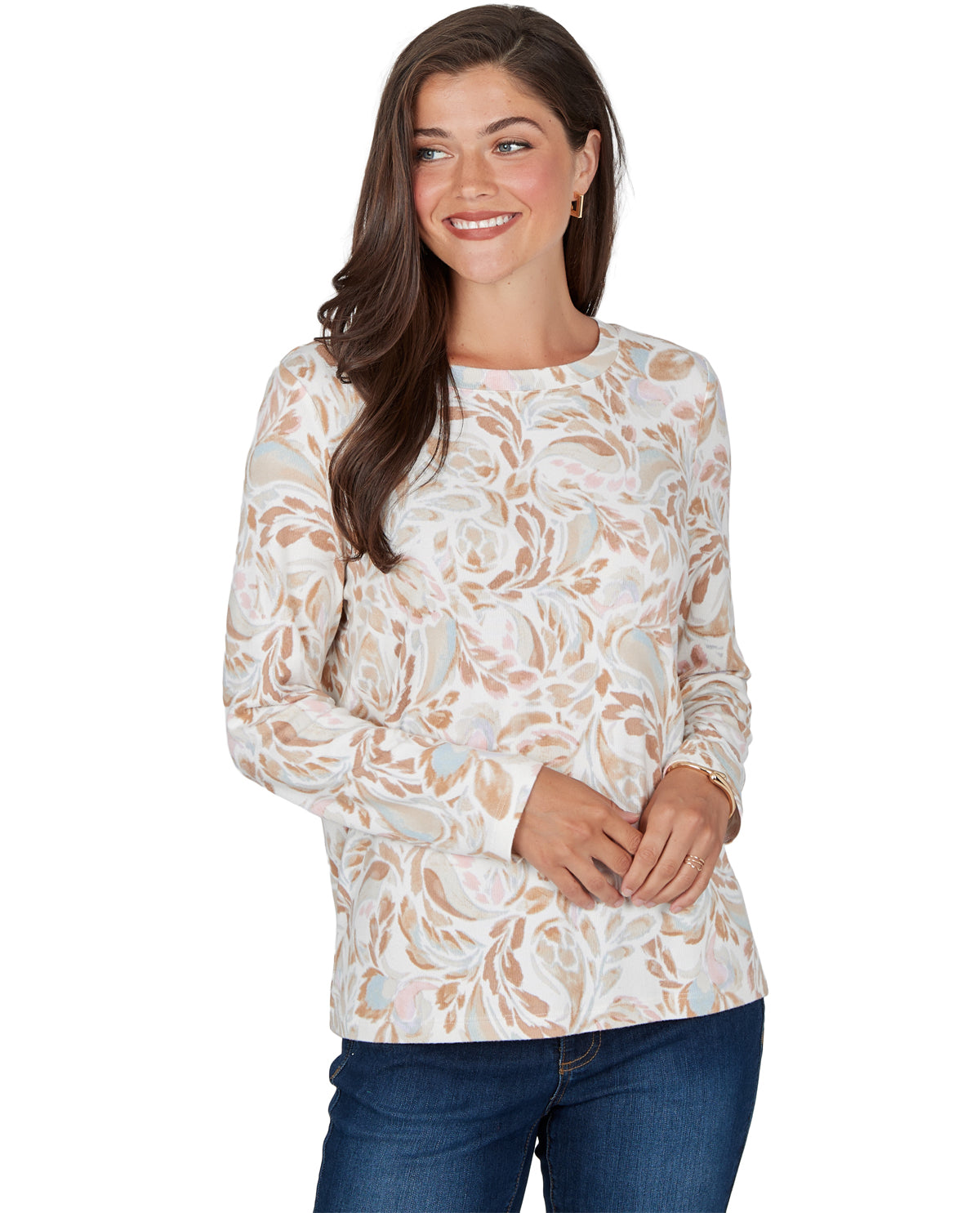 A woman modeling a long-sleeve crewneck top with an abstract floral pattern in beige, light blue, and white, paired with blue jeans against a plain white background.