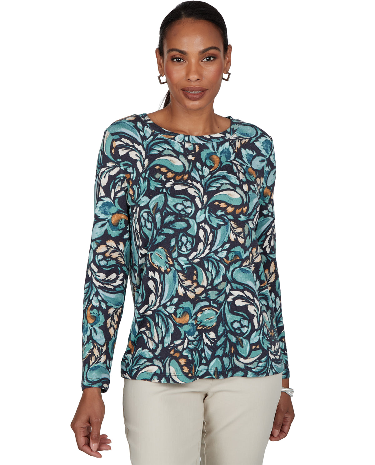 A woman modeling a long-sleeve top with an abstract floral pattern in teal, navy, white, and orange, paired with light beige pants, against a plain white background.
