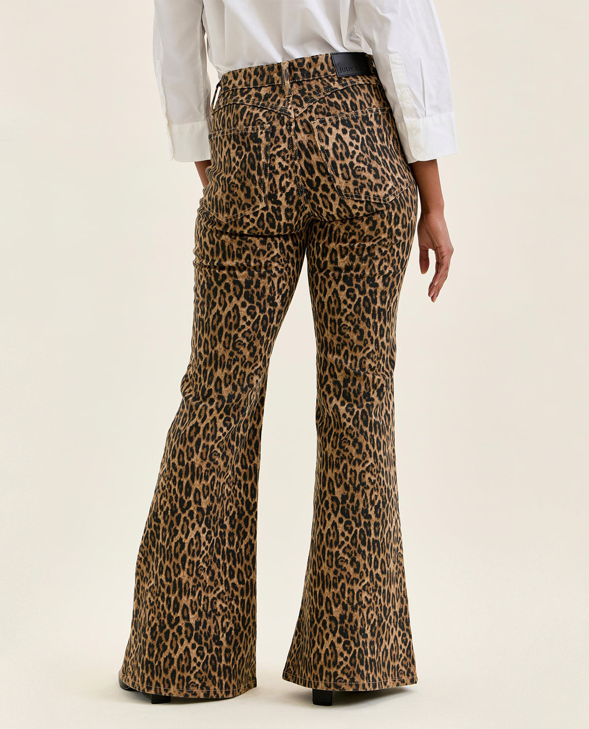 Leopard print flared pants worn by a person on a beige background