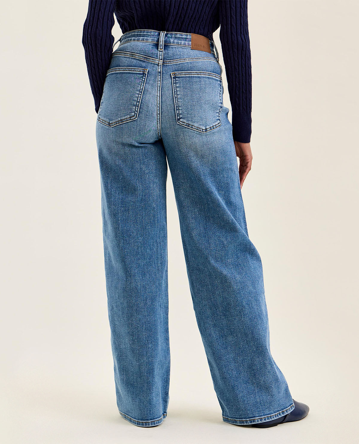 Person wearing blue jeans and a dark sweater on a plain background