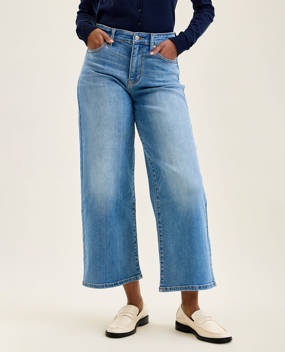 Person wearing blue jeans and white shoes on a plain background