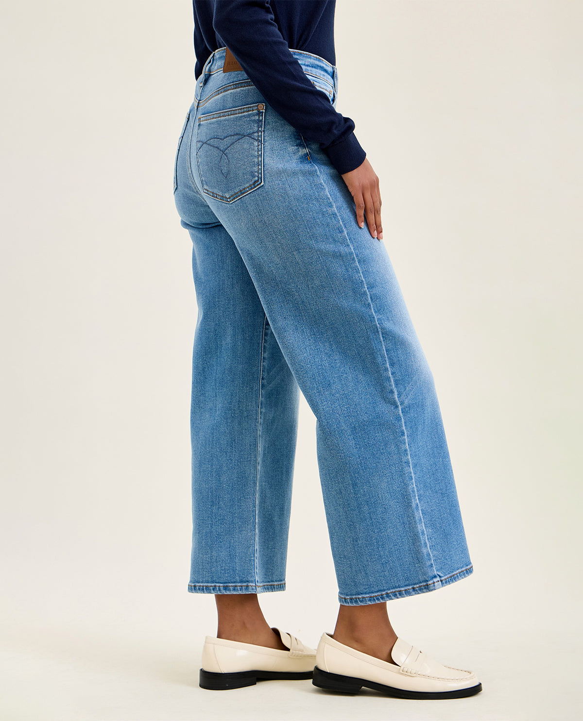 Person wearing blue jeans and white shoes on a plain background