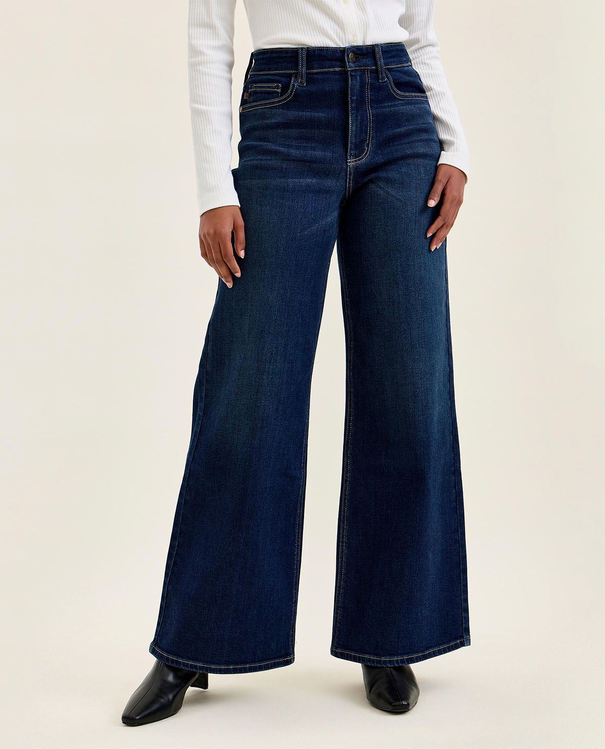 Person wearing dark blue flared jeans on a white background