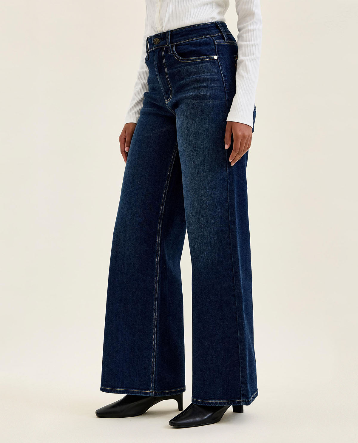 Person wearing dark blue wide-leg jeans on a beige background