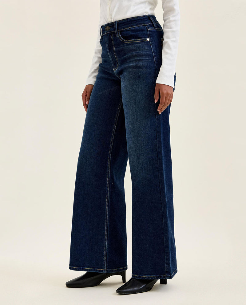Person wearing dark blue wide-leg jeans on a beige background