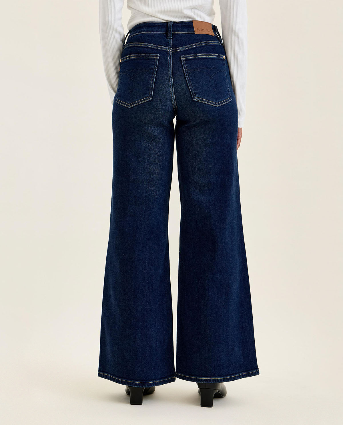 Person wearing dark blue wide-leg jeans on a beige background