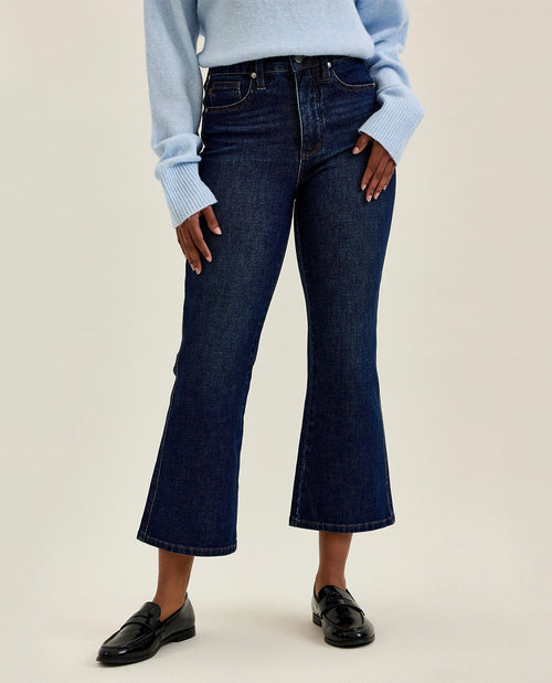 Person wearing dark blue flared jeans and a light blue sweater on a beige background