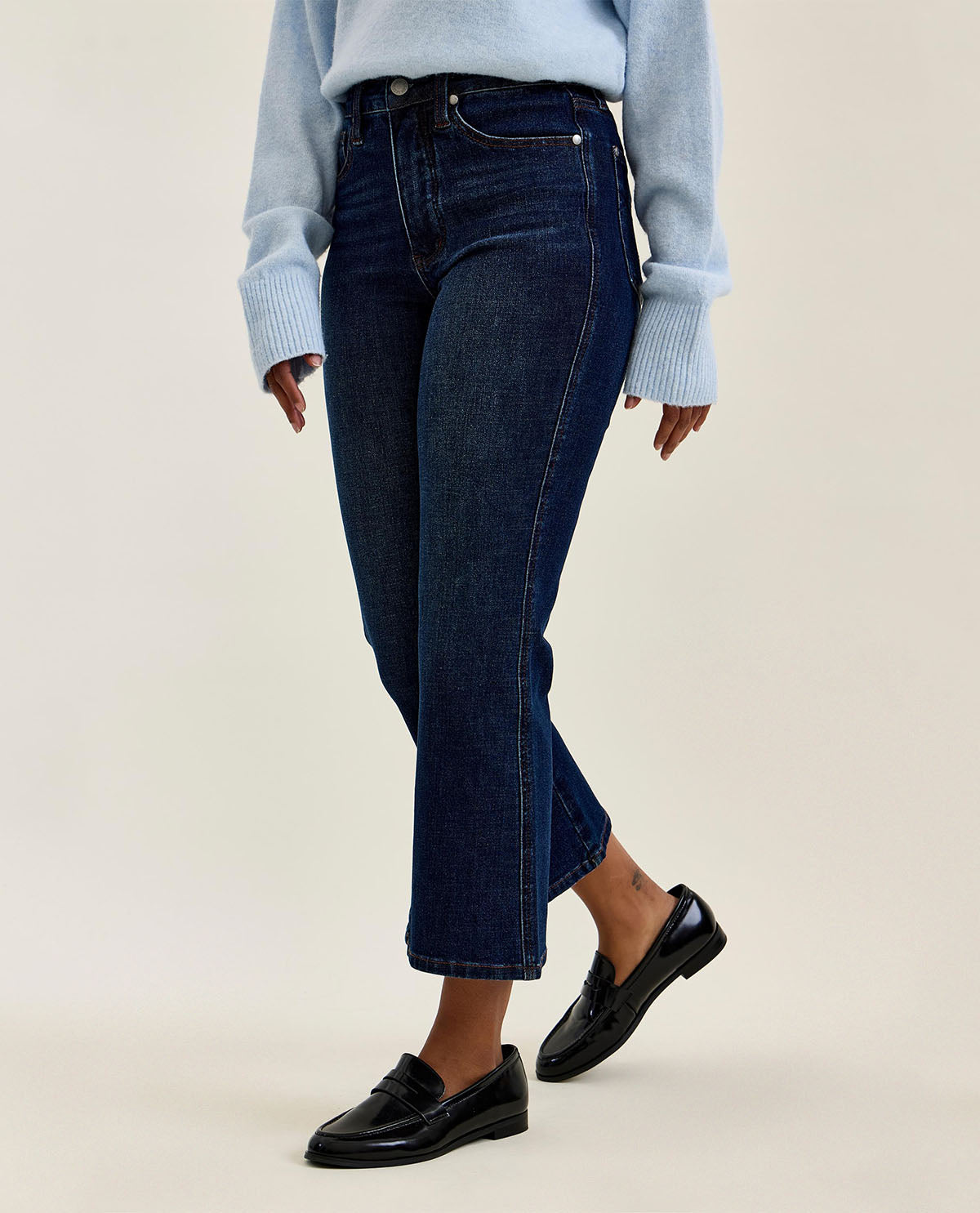 Person wearing dark blue jeans and black loafers on a beige background