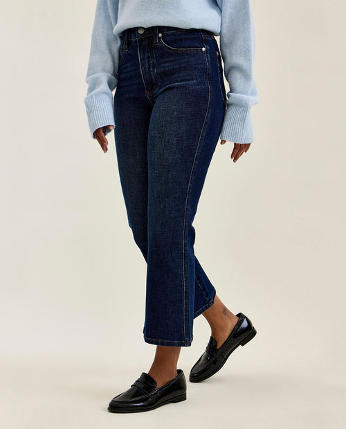 Person wearing dark blue jeans and black loafers on a beige background