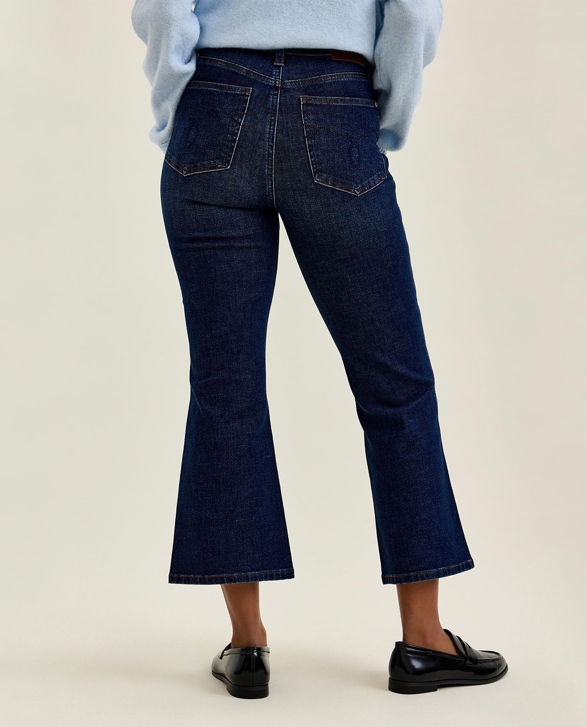 Person wearing dark blue flared jeans on a beige background