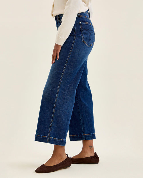Person wearing blue jeans and brown shoes on a white background