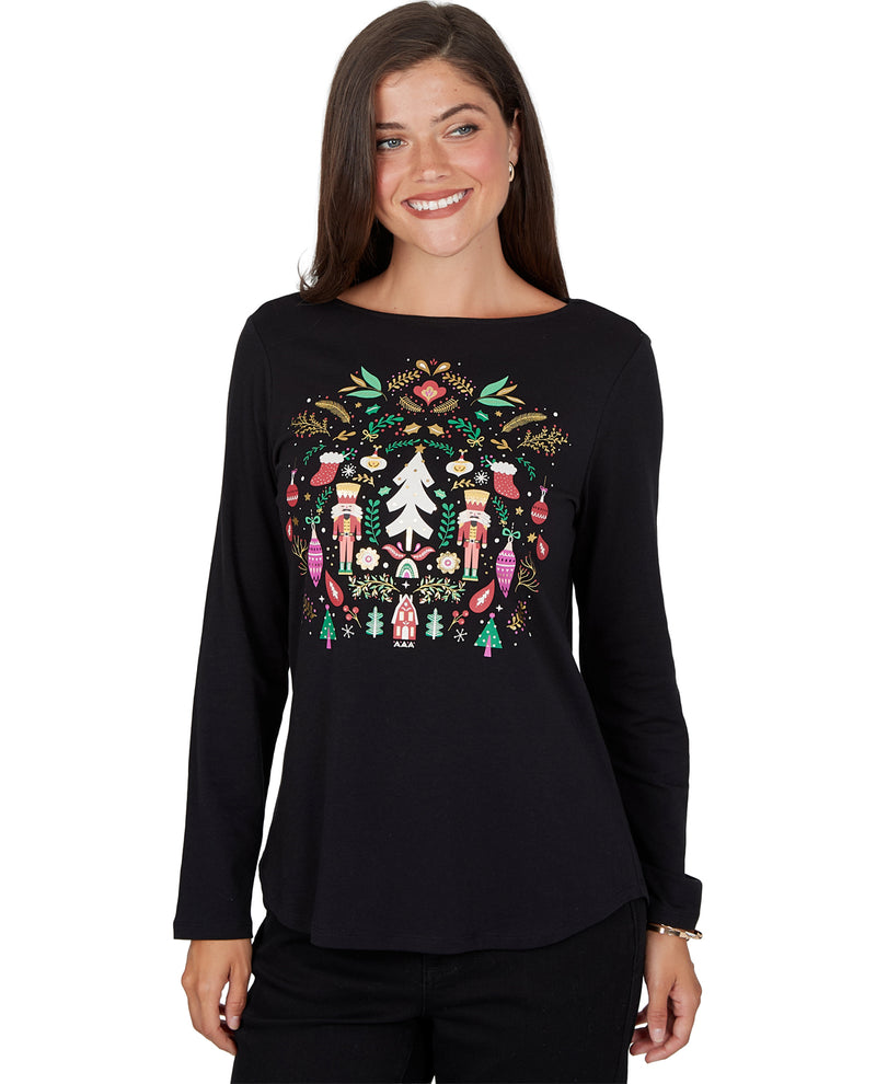 A woman wearing a black long-sleeve boatneck top with a colorful Christmas nutcracker graphic on the front, set against a plain white background.