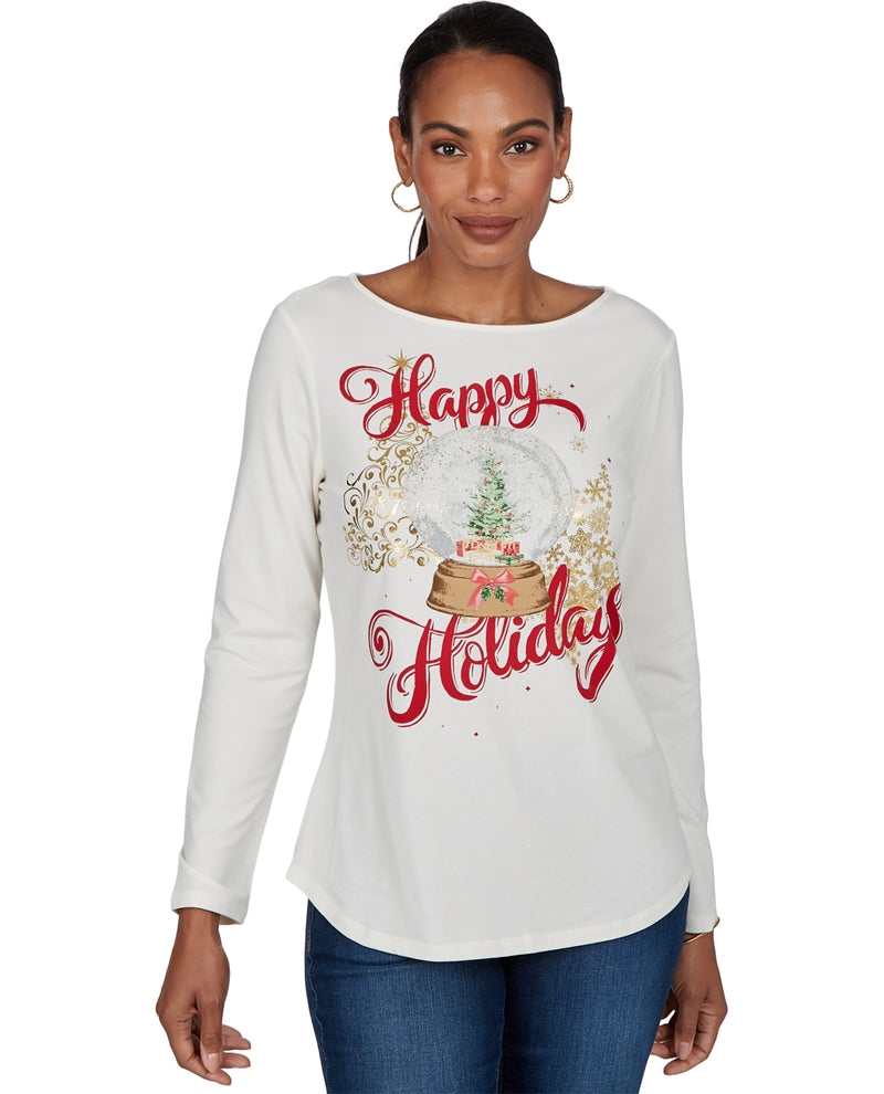 A woman modeling a white long-sleeve top with a 'Happy Holiday' snow globe graphic in red and gold, paired with blue jeans, against a plain white background.