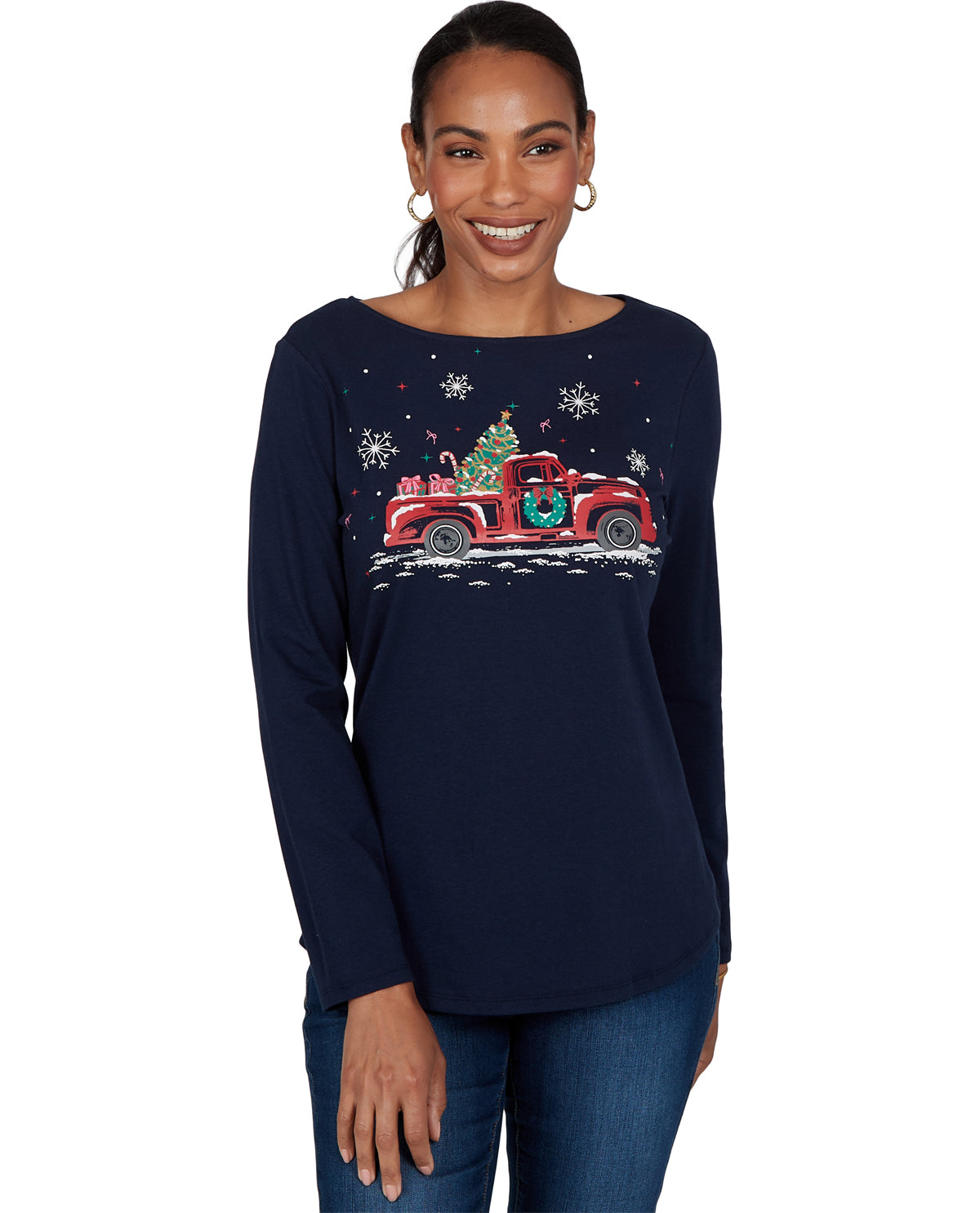 A woman wearing a navy blue long-sleeve boatneck top with a festive Christmas graphic of a red truck carrying a decorated tree, set against a plain white background.