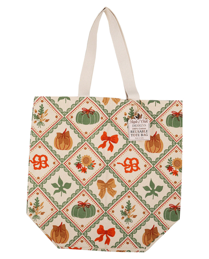 A reusable tote bag with a cream background and a diamond-patterned print featuring pumpkins, bows, leaves, and floral motifs in green, orange, and brown. The bag has two cream shoulder straps and a small white label on the front that reads 'Frigid Tree Designs Reusable Tote Bag'.