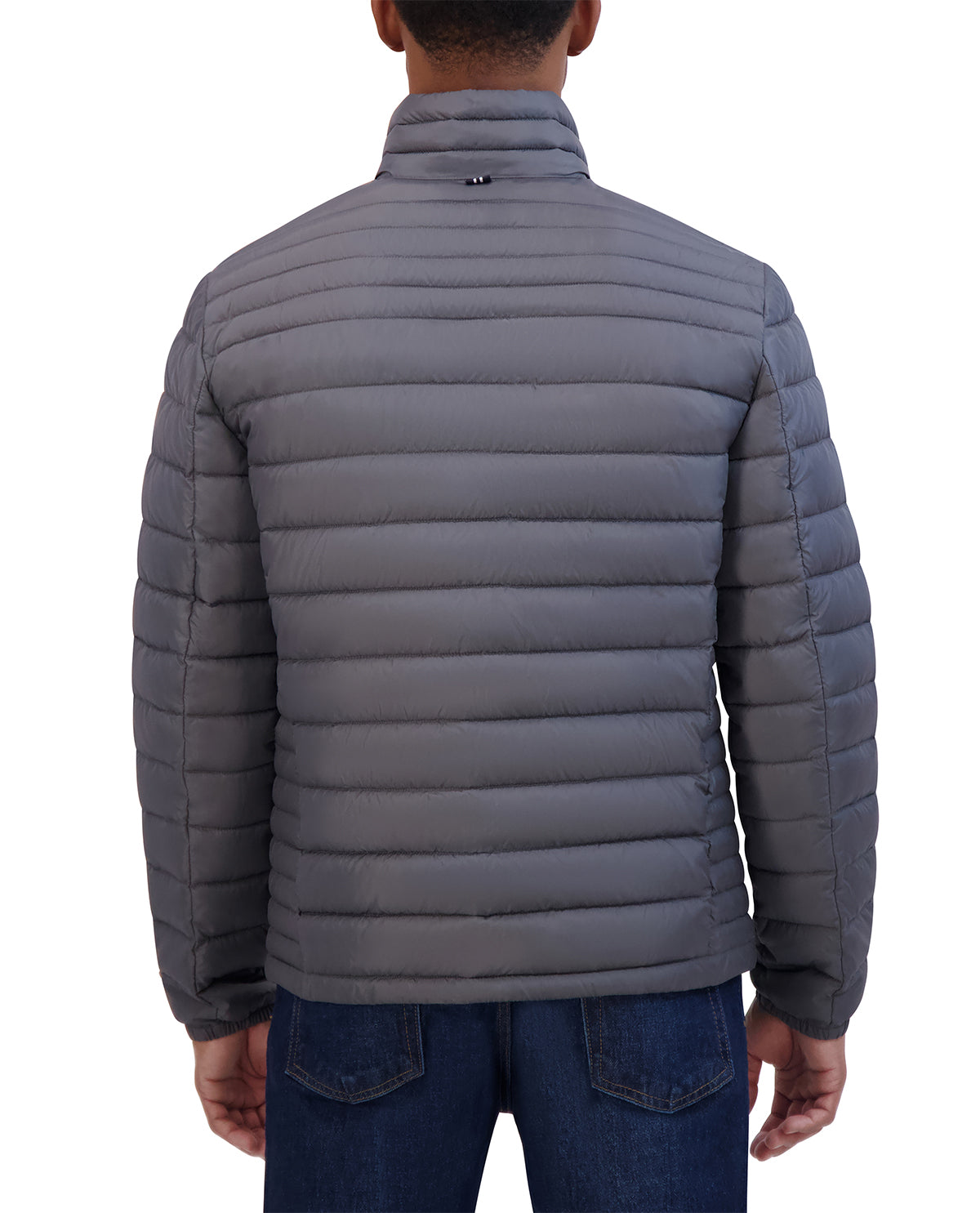 A man viewed from the back wearing a dark gray horizontally quilted puffer jacket and blue jeans against a plain white background.