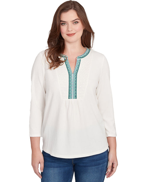 Woman wearing a white blouse with green embroidery on a white background