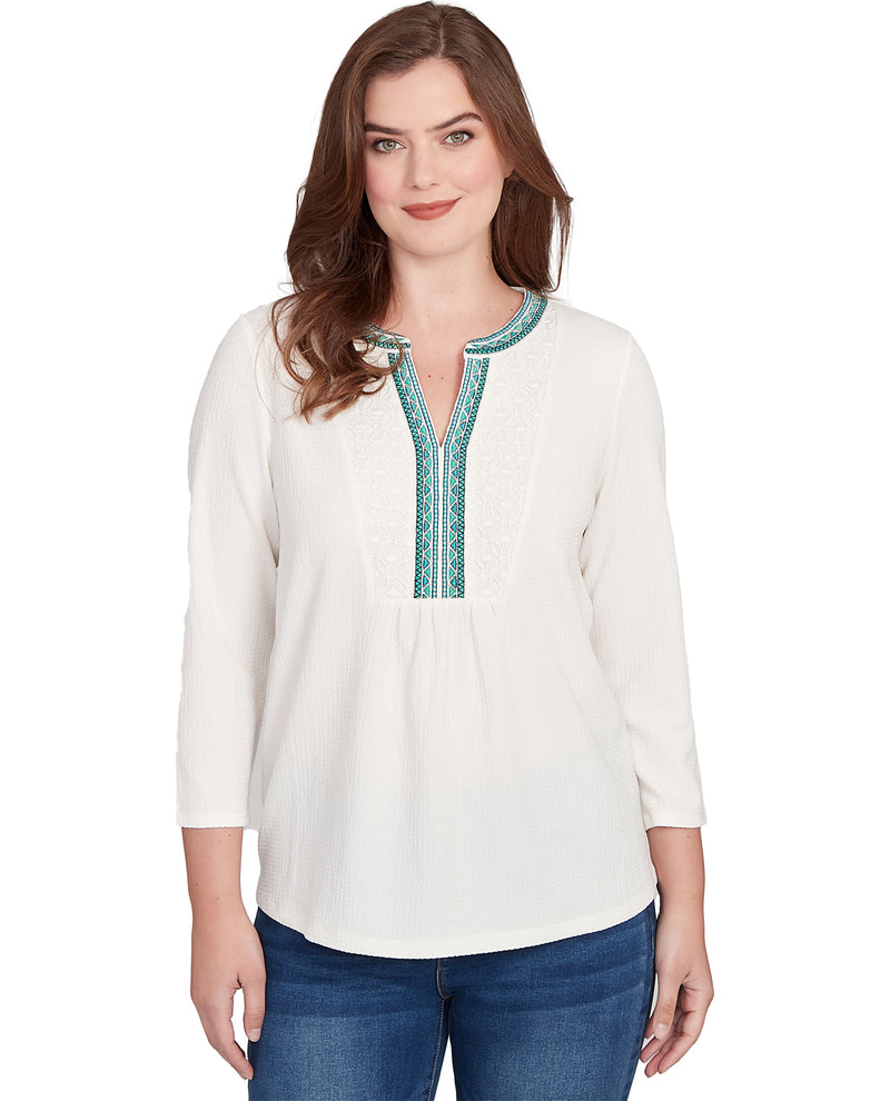 Woman wearing a white blouse with green embroidery on a white background