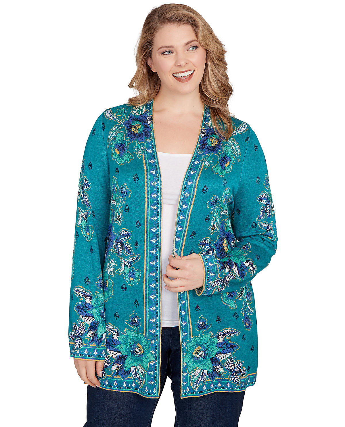 A woman modeling a teal open-front cardigan with blue and white floral embroidery and gold trim, worn over a white top and dark jeans against a plain white background.
