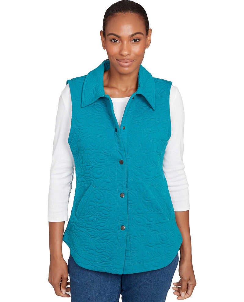 Woman wearing a teal quilted vest over a white long-sleeve shirt on a white background