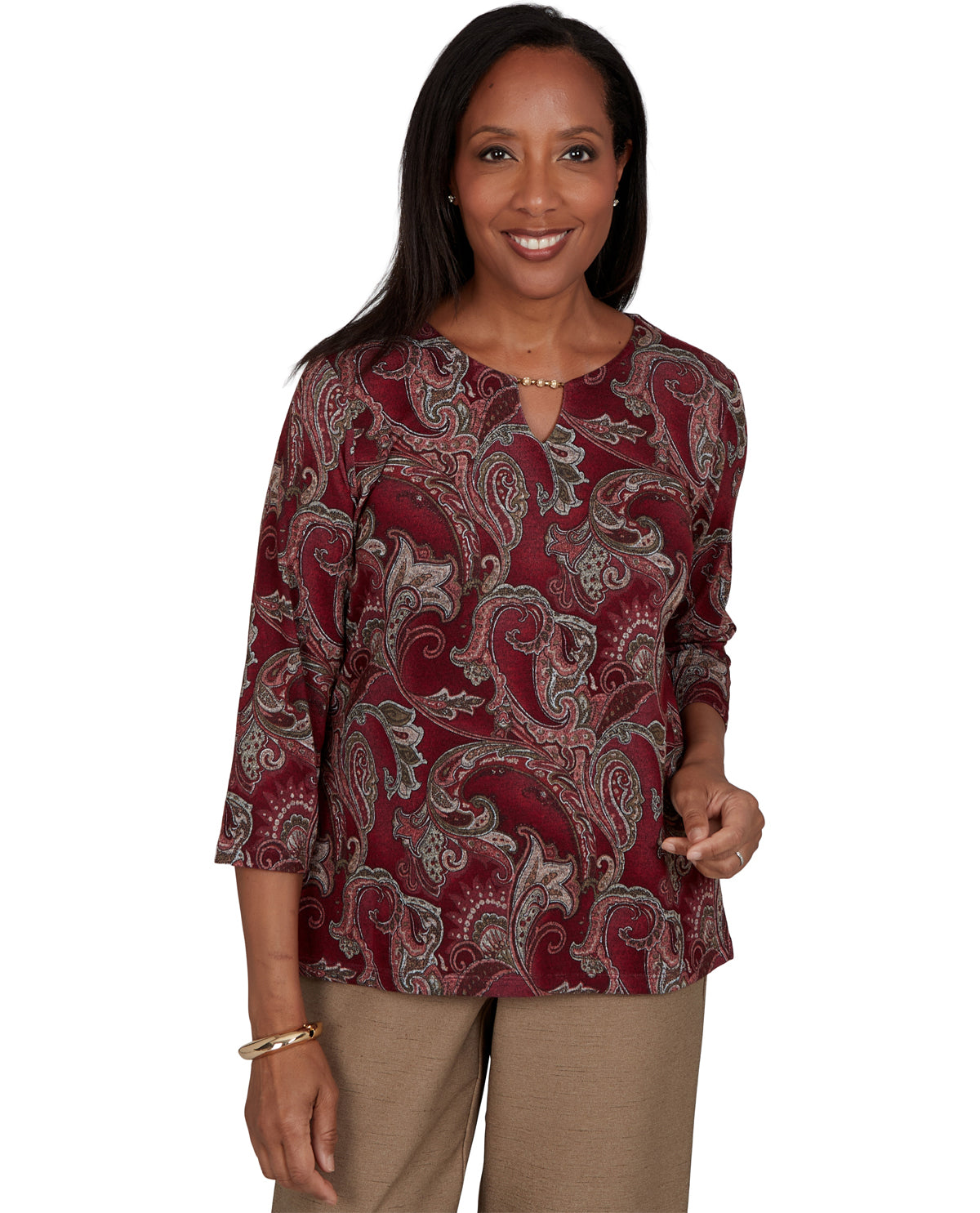 A woman modeling a three-quarter sleeve top with a burgundy paisley pattern and a split neckline, paired with tan pants, against a plain white background.