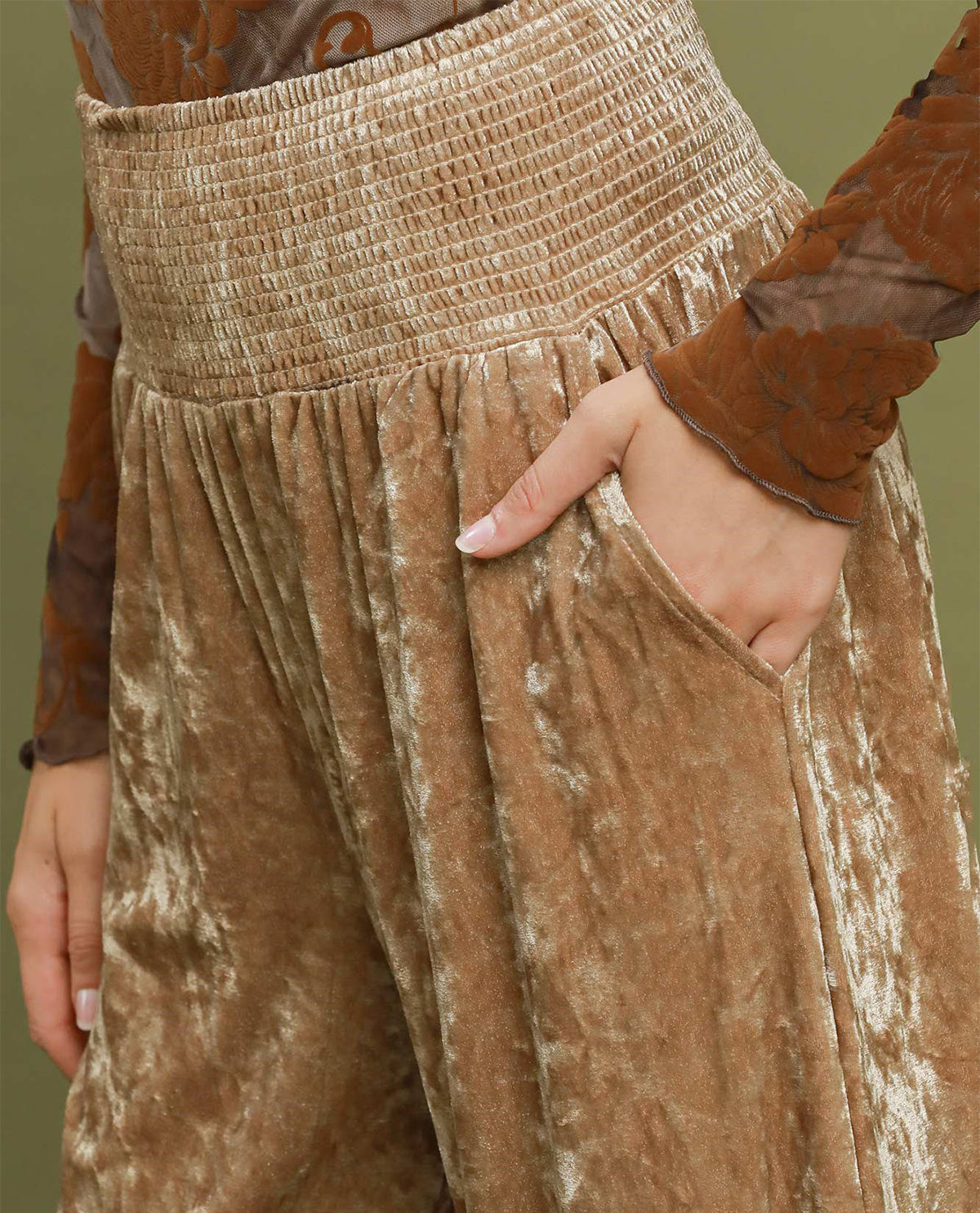 Close-up of a person wearing high-waisted, wide-leg trousers in a champagne gold crushed velvet fabric with a smocked waistband and side pockets.