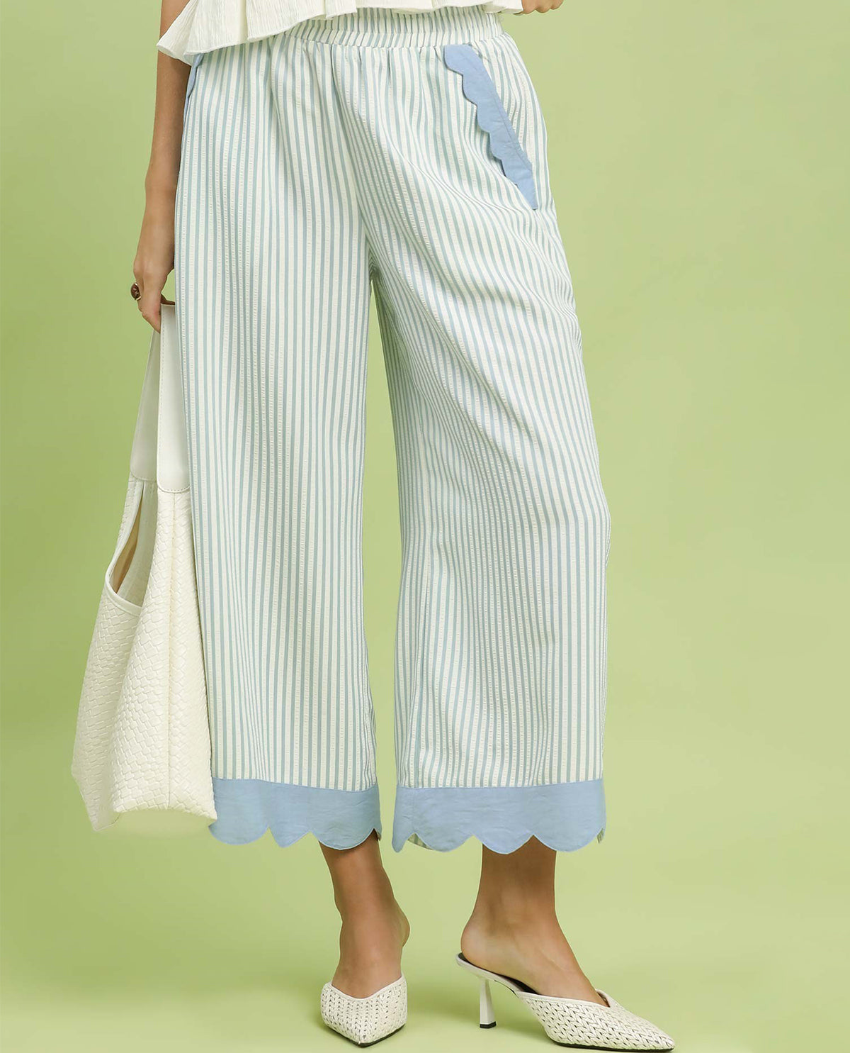 Woman wearing light blue and white striped pants with scalloped hem on a green background