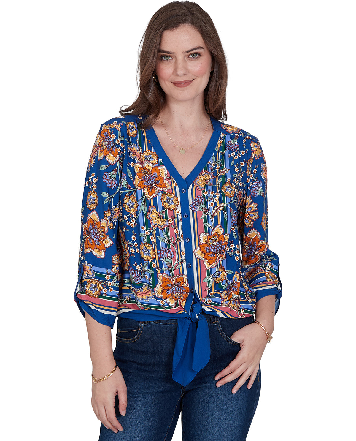 A woman modeling a blue floral and striped long-sleeve blouse with a V-neck and tie-front detail, paired with dark blue jeans, against a plain white background.