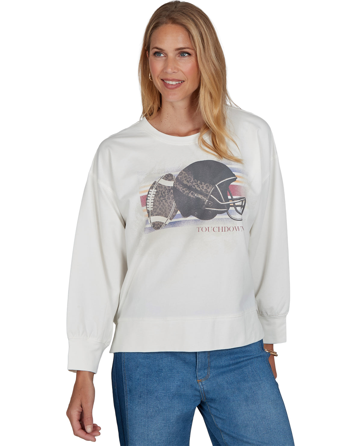A woman wearing a white long-sleeve crewneck sweatshirt with a graphic of a football helmet and football on the front, paired with blue jeans, against a plain white background.