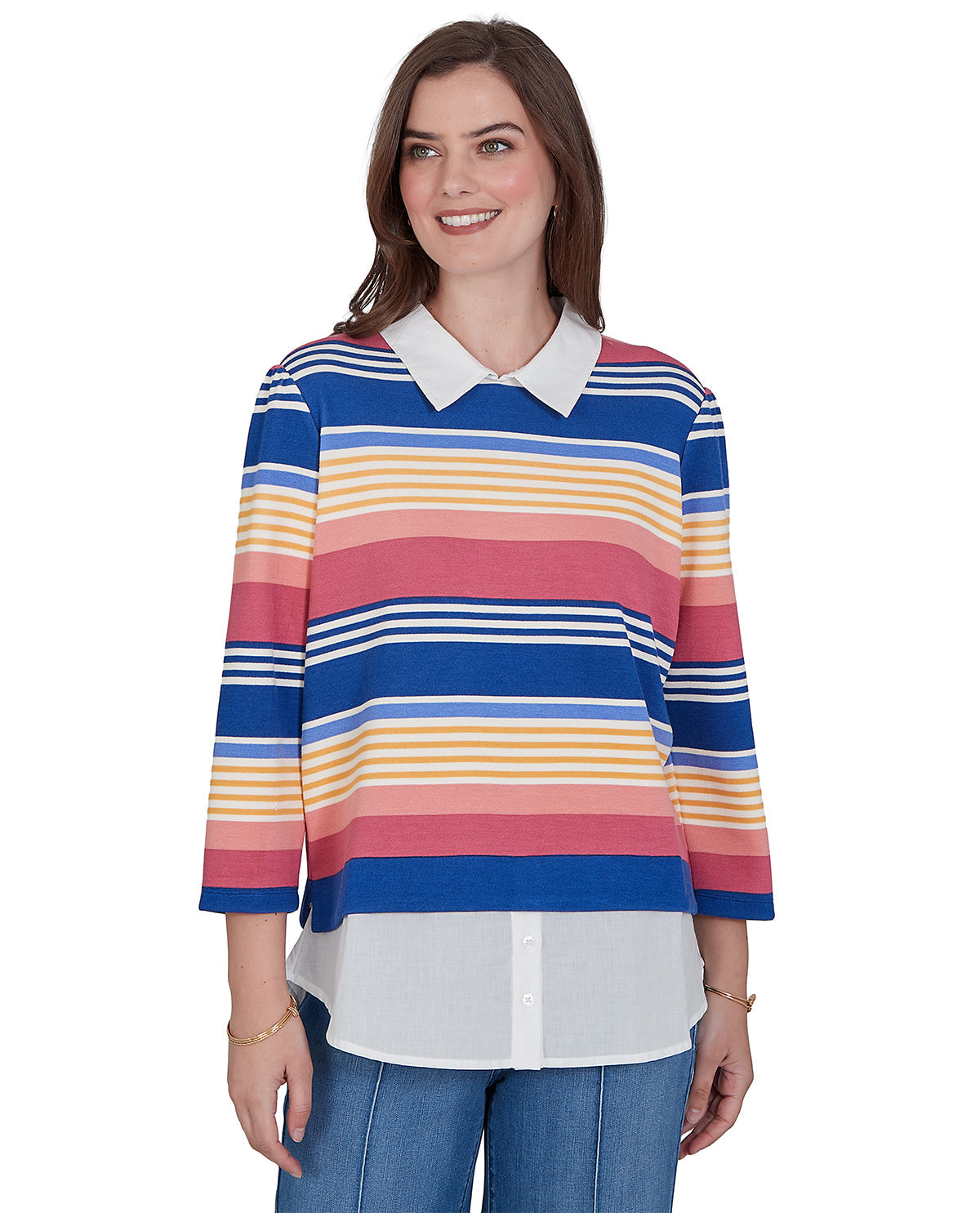 A woman modeling a long-sleeve collared knit top with horizontal stripes in blue, pink, yellow, and white, paired with blue jeans against a plain white background.